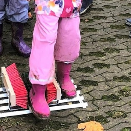 Kinder reinigen Stiefel mit dem Schuhreiniger - Fußabtreter mit Bürsten und Gitterrost im Außenbereich.