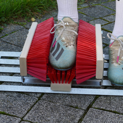 Fußballschuhe werden auf einem Schuhabtreter mit Bürsten gereinigt.