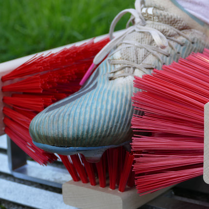 Stollen der Fußballschuhe werden auf einem Schuhabtreter mit Bürsten gereinigt. 